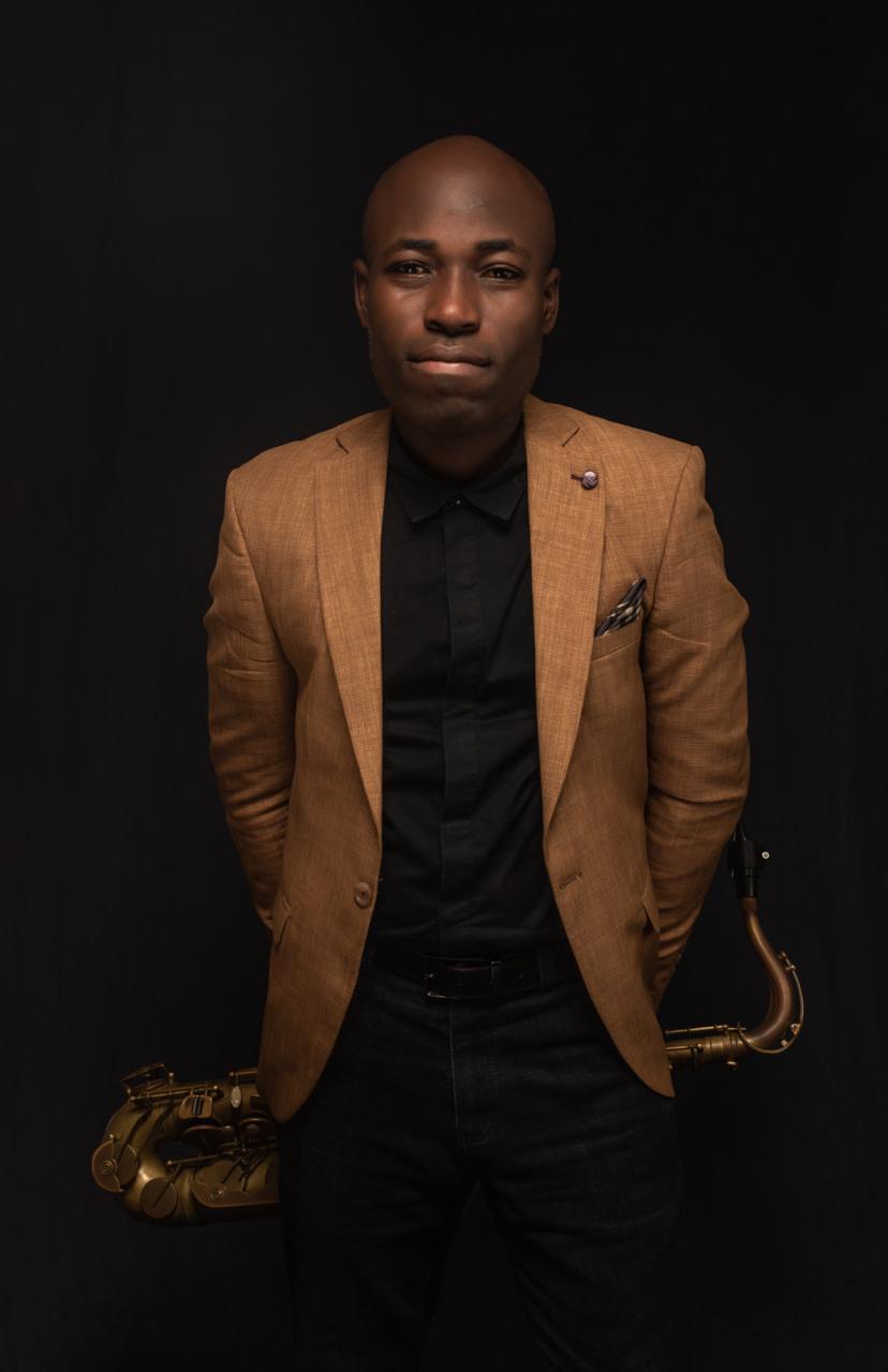 Emmanuel Atoyebi in a brown jacket holding his saxophone